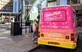 Rear view of a custom vinyl wrapped iMP sampling van featuring vibrant pink and orange branding for a cosmetics roadshow