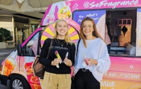 Smiling target audience consumers holding physical product samples and digital discount codes at an iMP fragrance roadshow