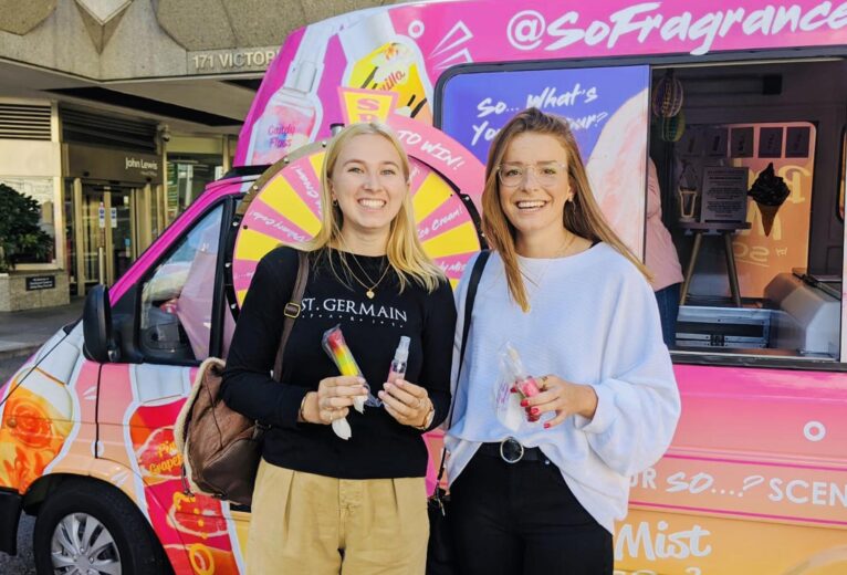 Smiling target audience consumers holding physical product samples and digital discount codes at an iMP fragrance roadshow