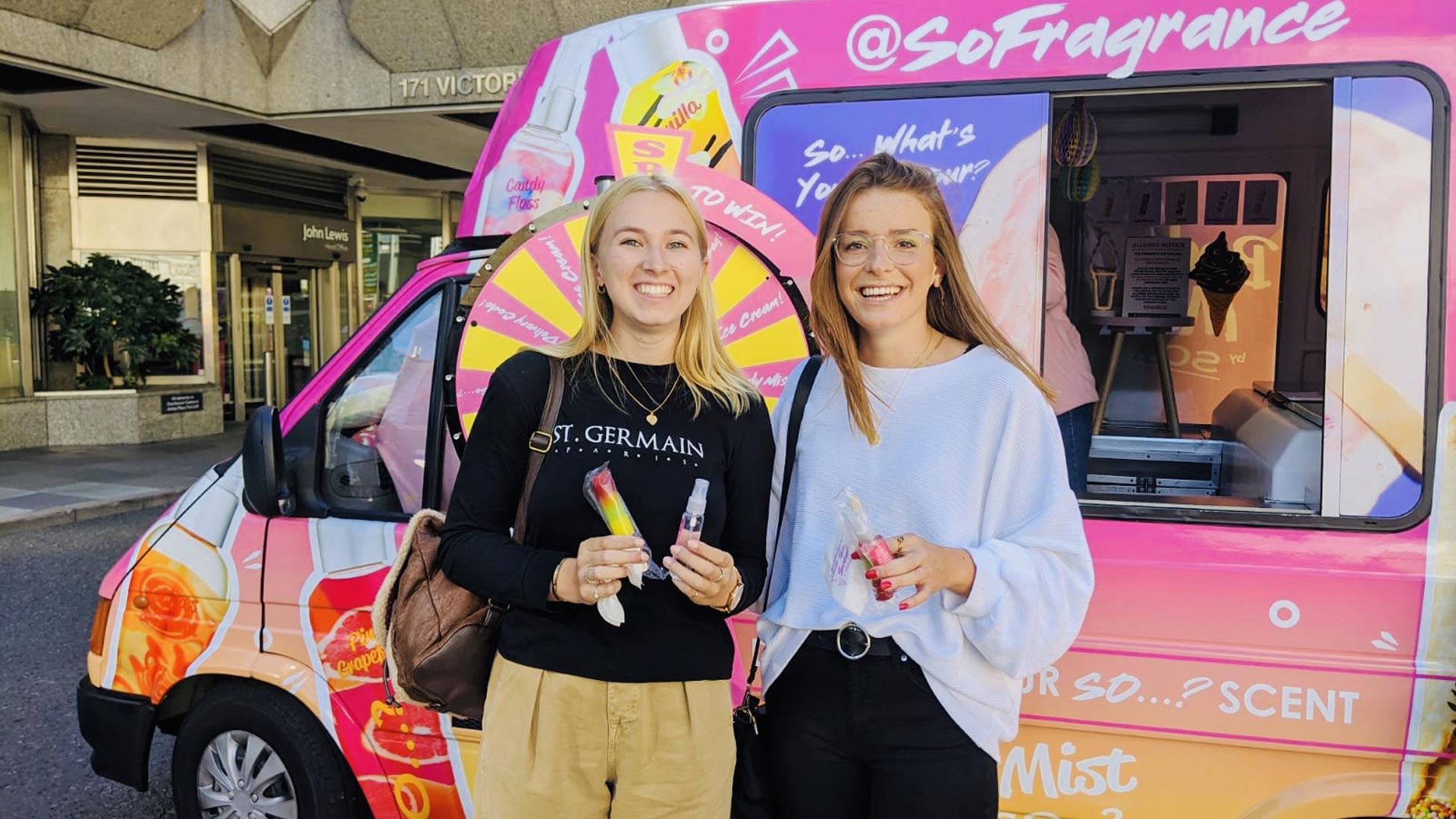 Smiling target audience consumers holding physical product samples and digital discount codes at an iMP fragrance roadshow