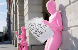 Pink morph suit Flo App reading newspaper in London